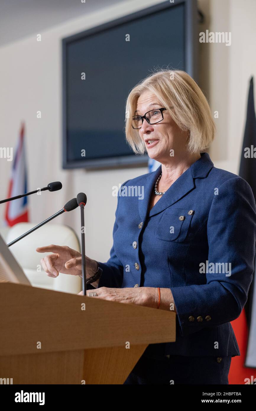 Déléguée féminine mature debout par Tribune à la conférence politique et faisant rapport à des collègues étrangers Banque D'Images