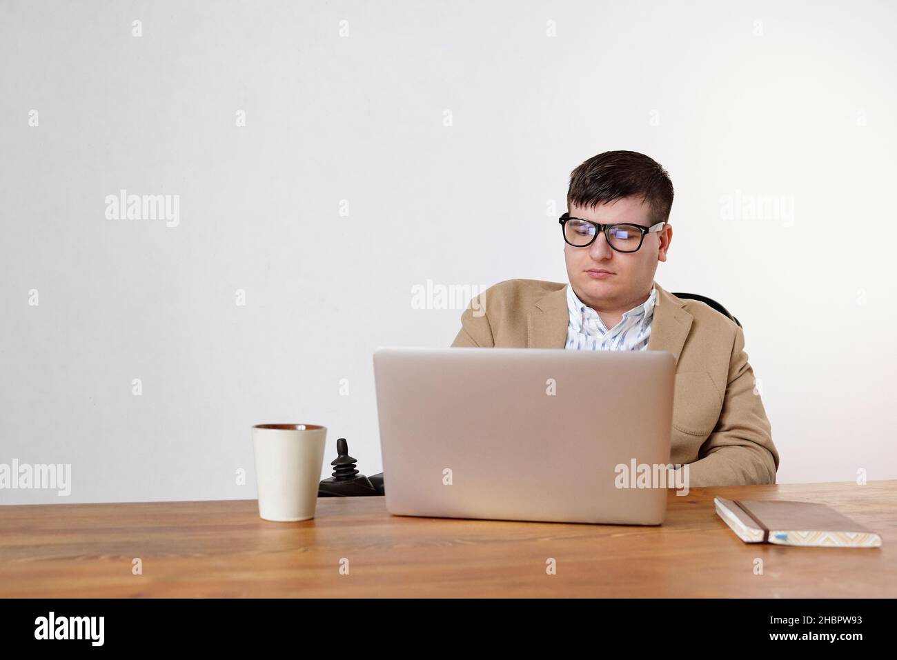 Homme d'affaires sérieux avec un handicap regardant l'écran d'un ordinateur portable tout en se connectant au bureau contre un mur blanc Banque D'Images