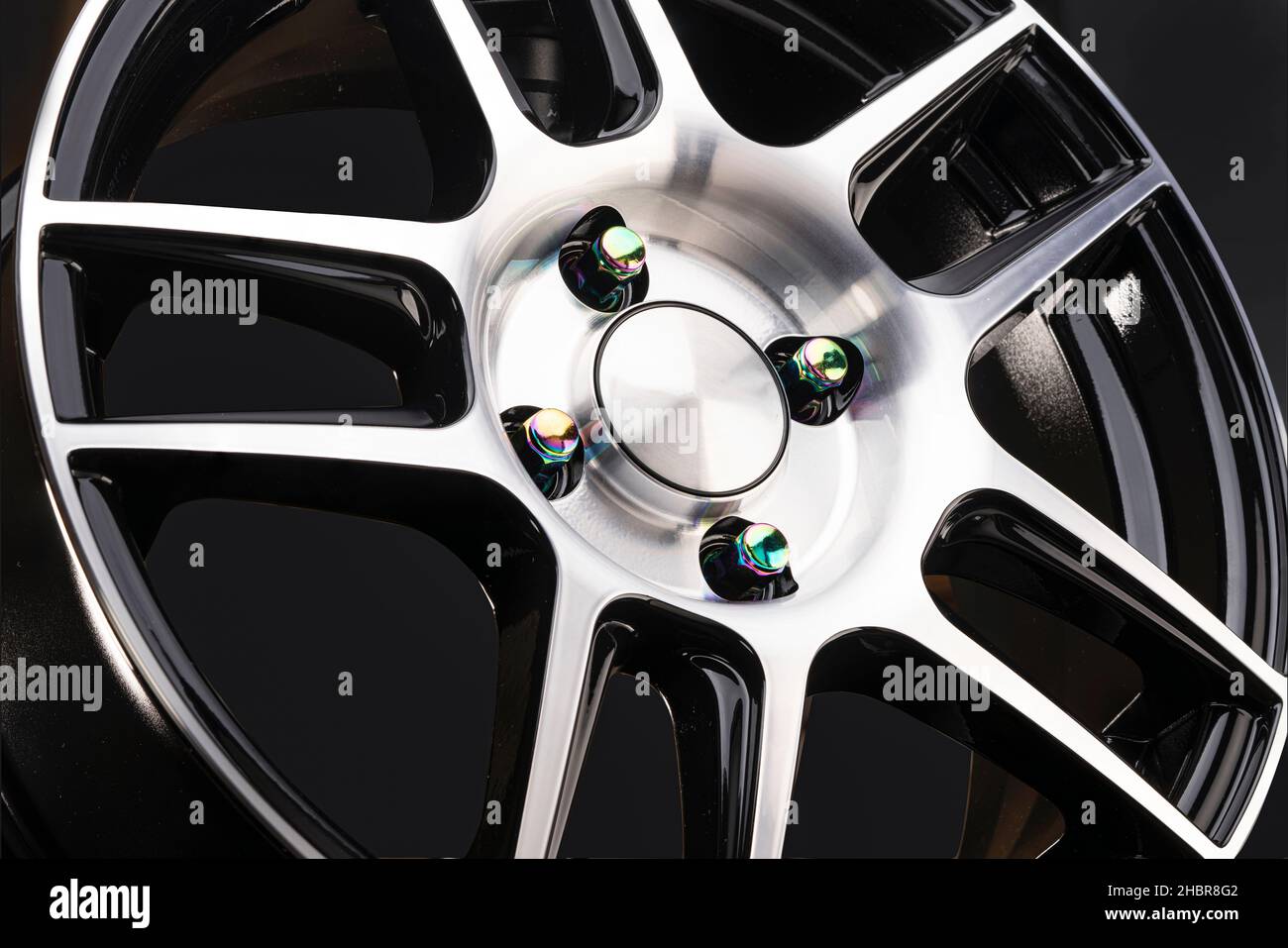 roue en alliage légère et sportive avec branches et jante à poutres fines, avec de magnifiques noix de caméléon de couleur multicolore arc-en-ciel sur un fond noir. Banque D'Images