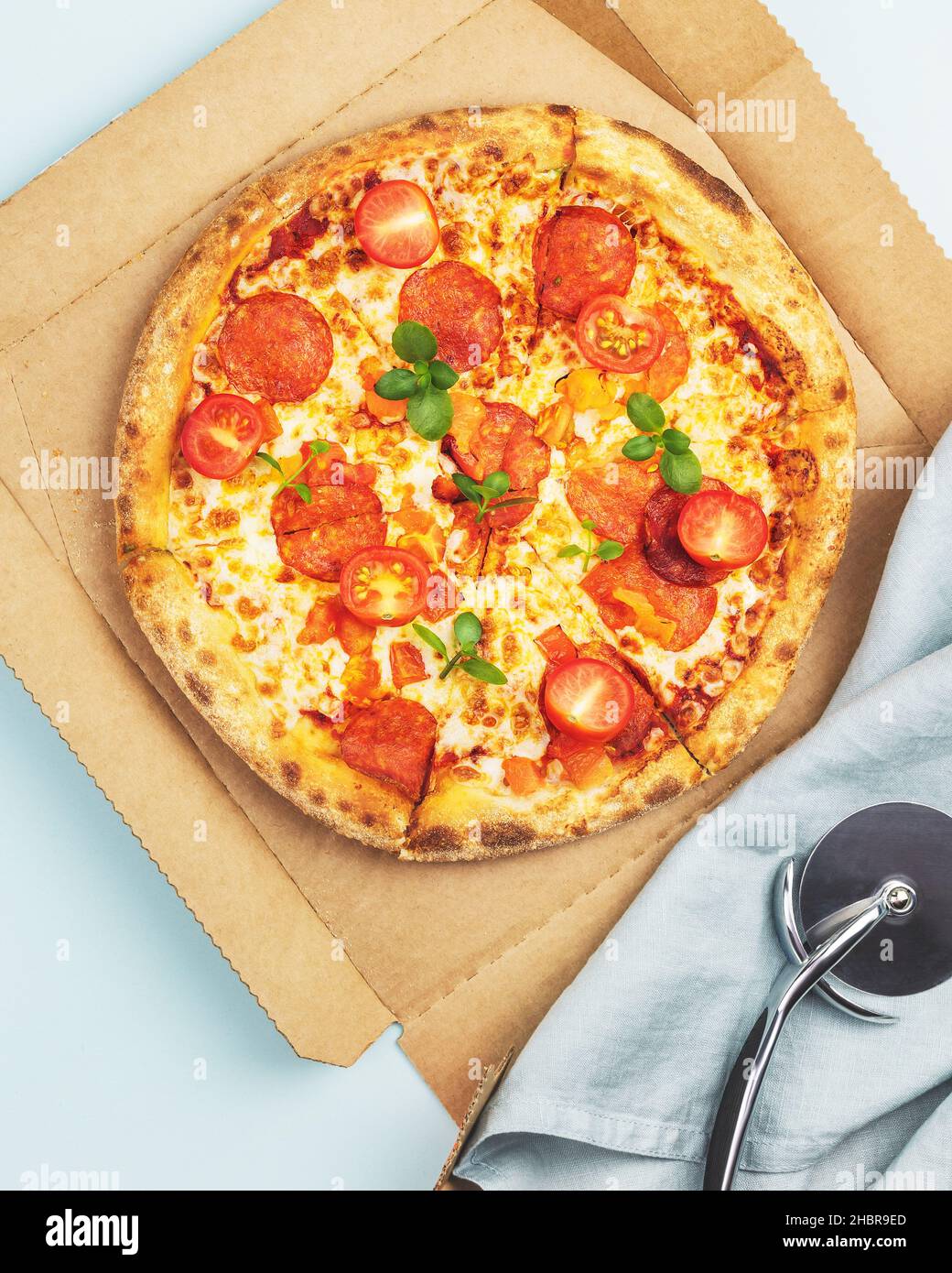 Savoureuse grande pizza italienne au pepperoni avec une fine pâte, salami, mozzarella, tomates cerises et basilic dans une boîte artisanale sur fond bleu avec espace de copie. Banque D'Images