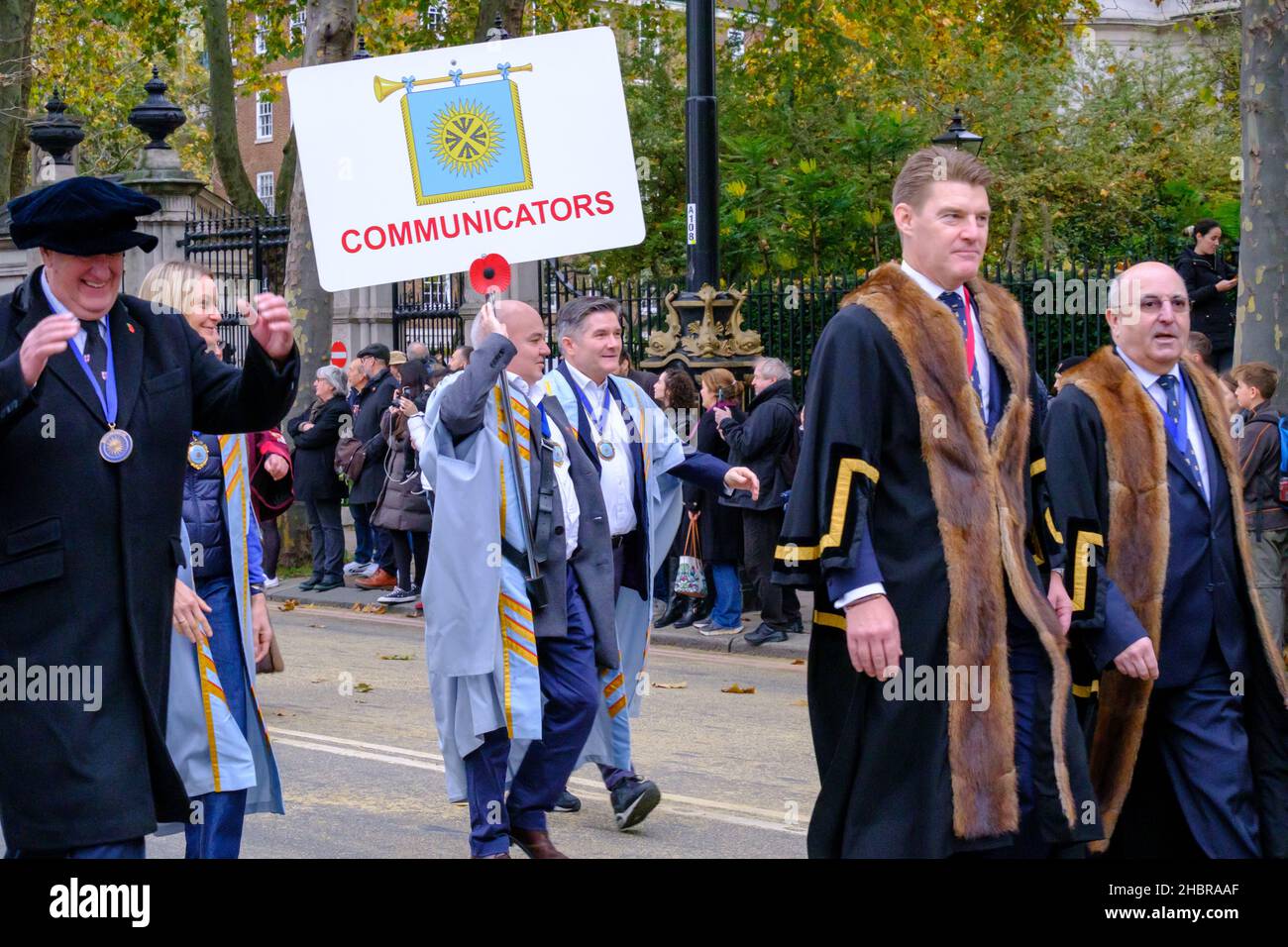 Hommes et femmes dans des robes de cérémonie, tenant un signe de communication, marche avec les compagnies modernes de Livery dans le Lord Mayor’s Show 2021, Londres. Banque D'Images