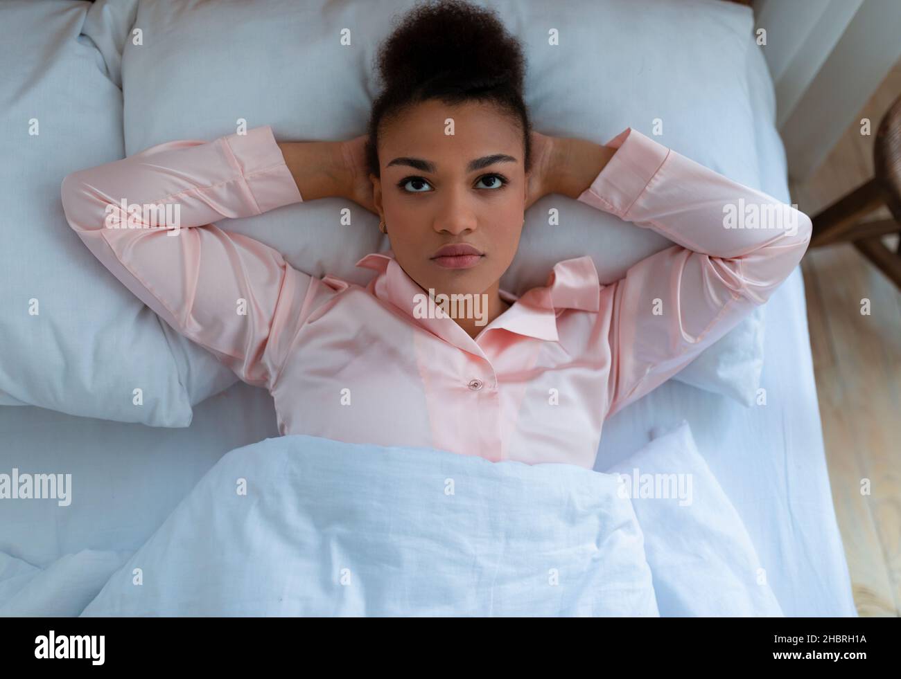 Femme afro-américaine fatiguée souffrant de dépression et de stress, allongé sur un lit blanc à la maison, vue de dessus Banque D'Images