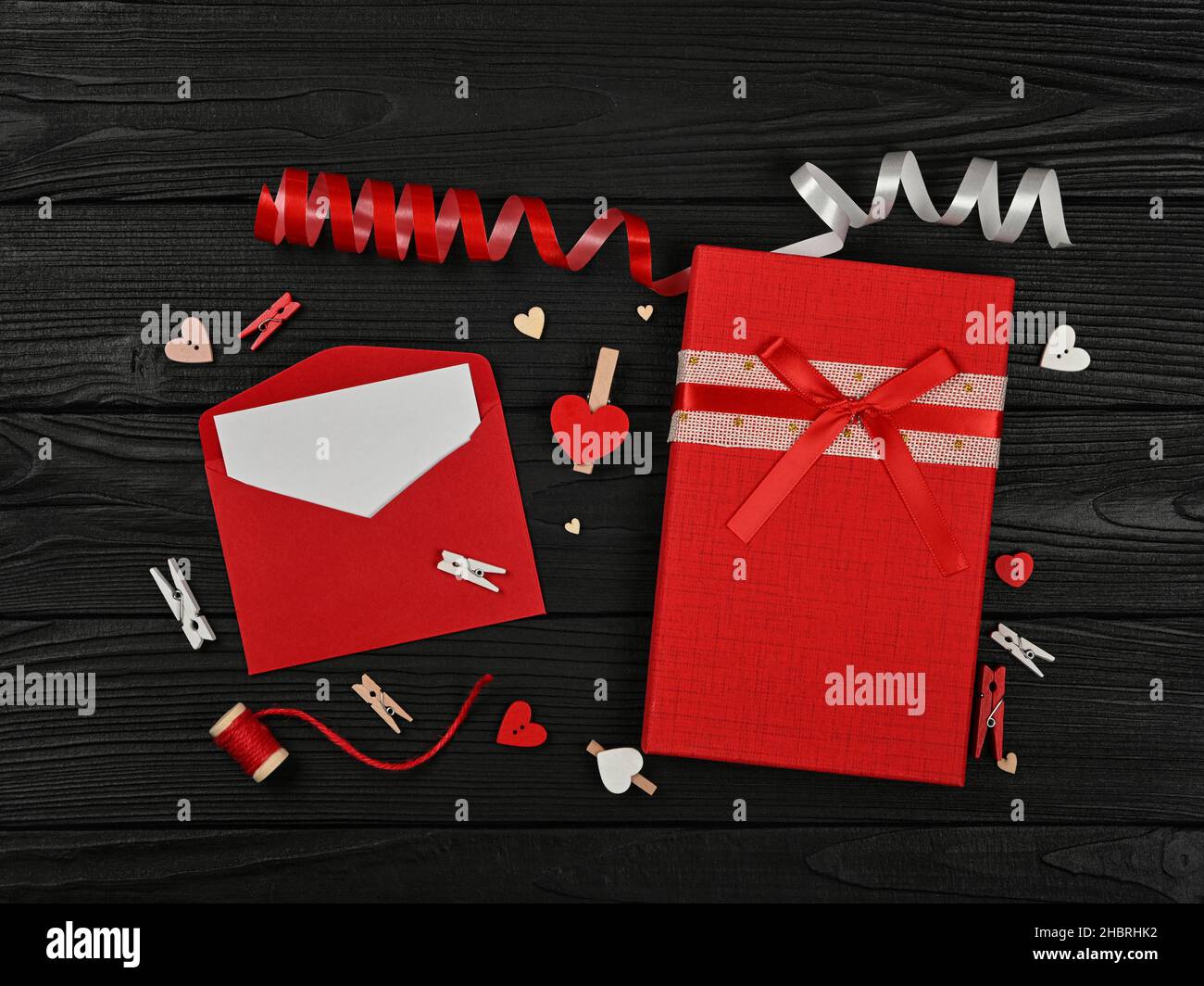 Préparer des cadeaux de Saint-Valentin, des boîtes rouges, des coeurs, de la ficelle, des épingles à linge et une note dans une enveloppe en papier sur fond de table en bois noir, pose à plat rapprochée, eleva Banque D'Images