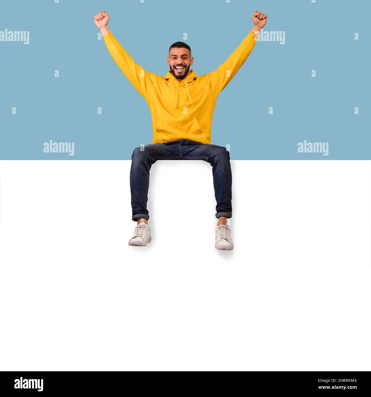 Modèle de panneau publicitaire.Un homme arabe excité assis au-dessus d'une affiche blanche vierge avec une maquette, levant les mains Banque D'Images