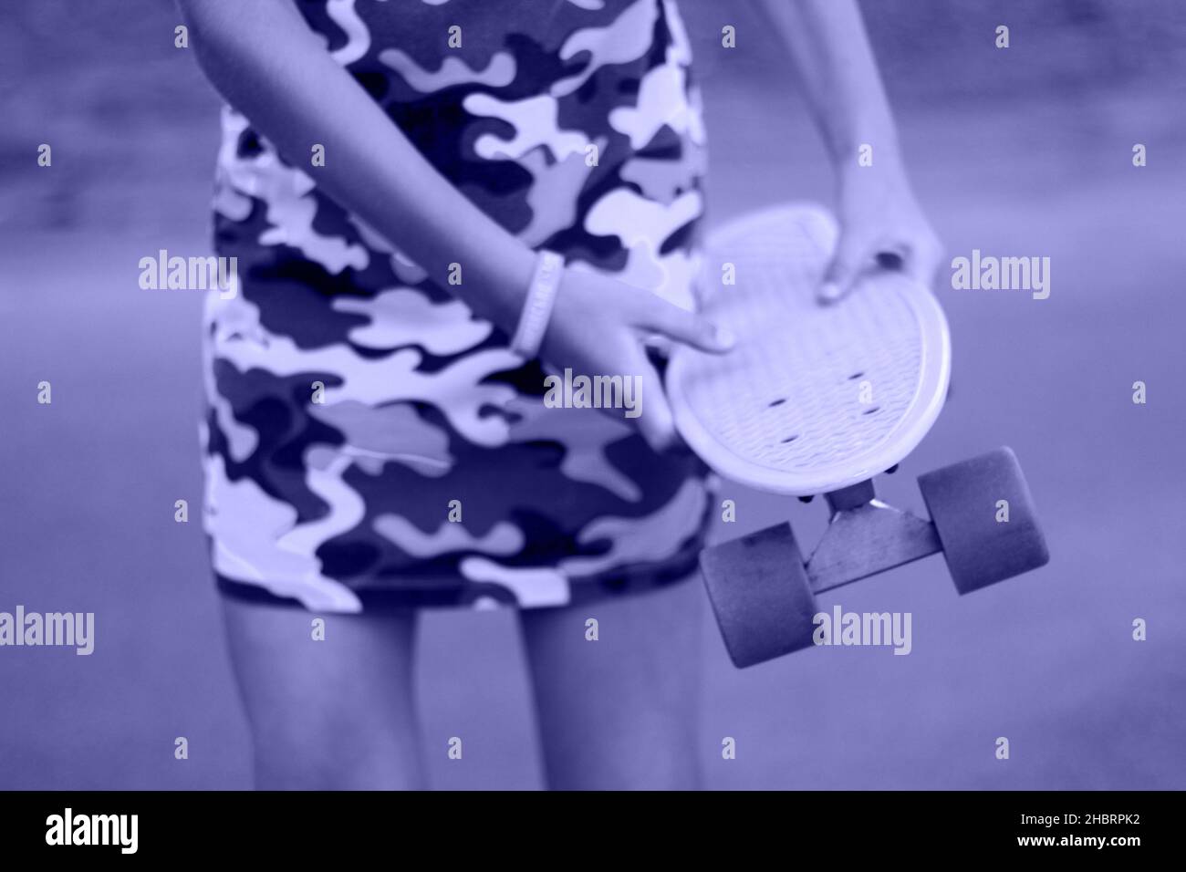 Défocus fille tenant un panneau jaune de penny.Vue avant.Culture des vêtements hipster pour jeunes.Les mains des enfants tiennent un petit panneau de promenade de croiseur à l'extérieur pendant la journée.Couleur du Banque D'Images