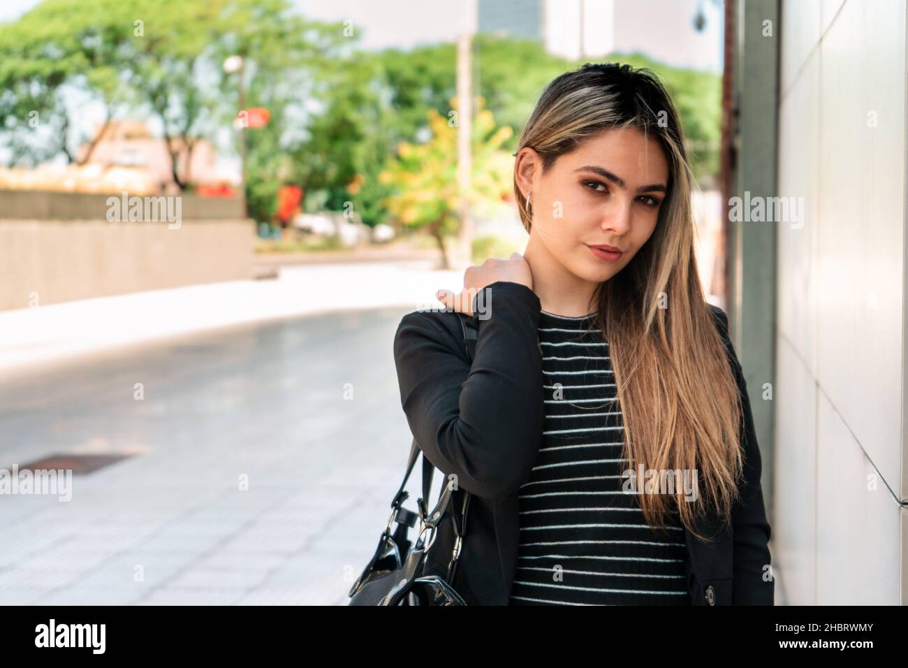 Belle femme entreprenante debout avec une expression sérieuse par le mur d'un immeuble de bureau sur une journée ensoleillée. Banque D'Images