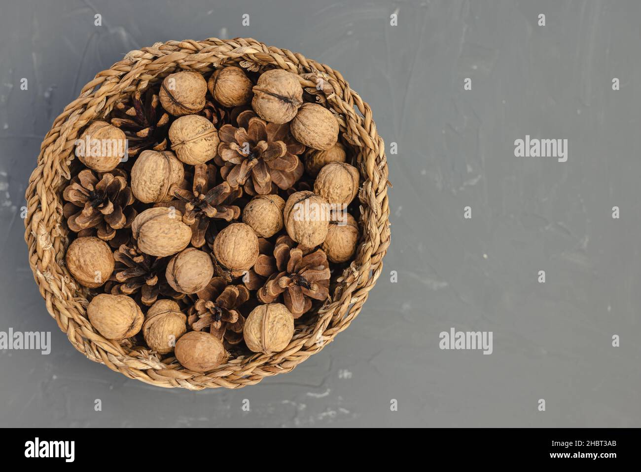Noix crues en carapace et cônes de pin en panier comme décoration de table d'automne ou de Noël sur fond gris foncé.Vue de dessus, espace de copie Banque D'Images