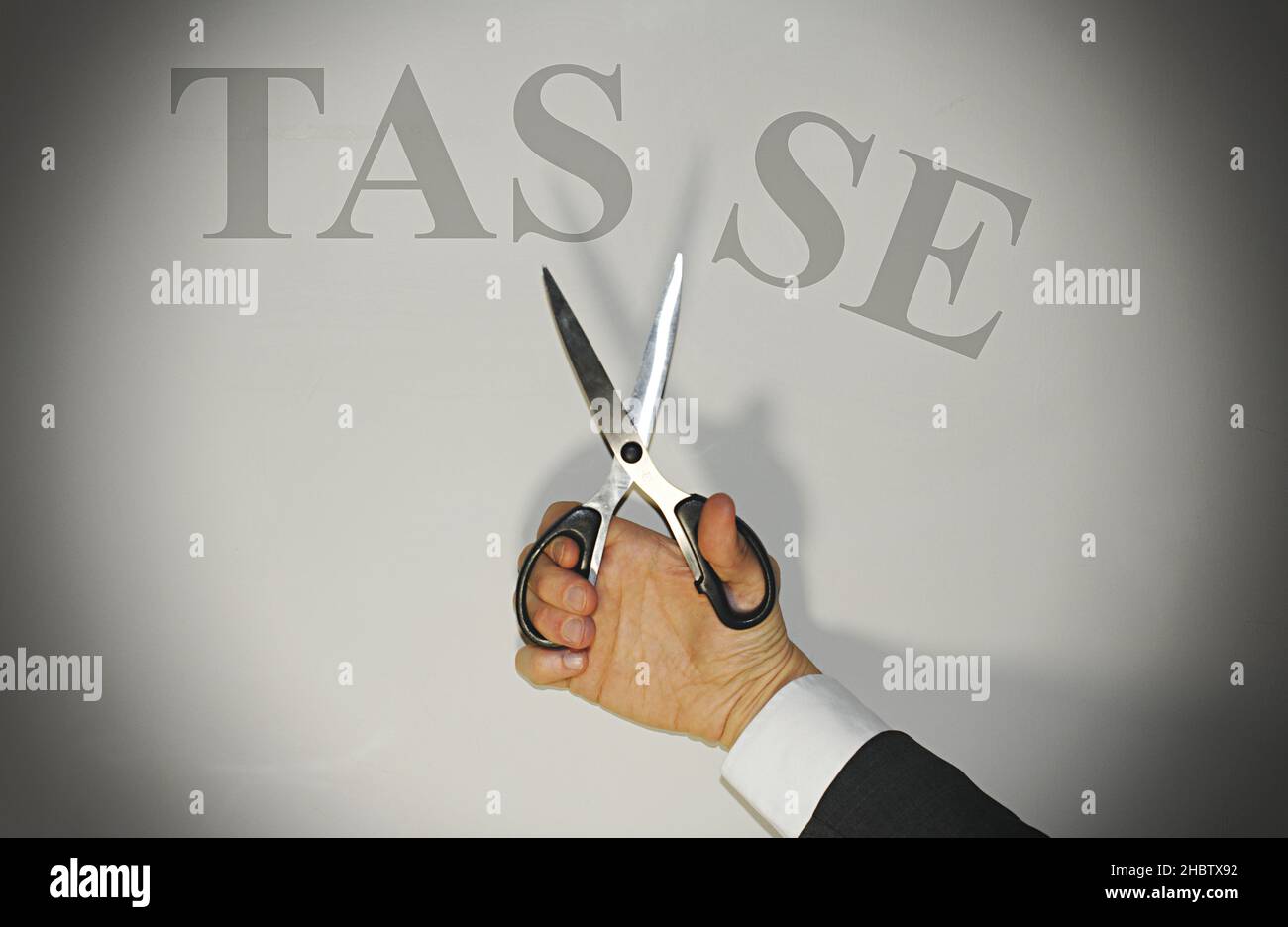 Main tenant des ciseaux coupant le mot 'Tasse' traduisant en impôts italiens, concept de réduction de la fiscalité en Italie. Banque D'Images