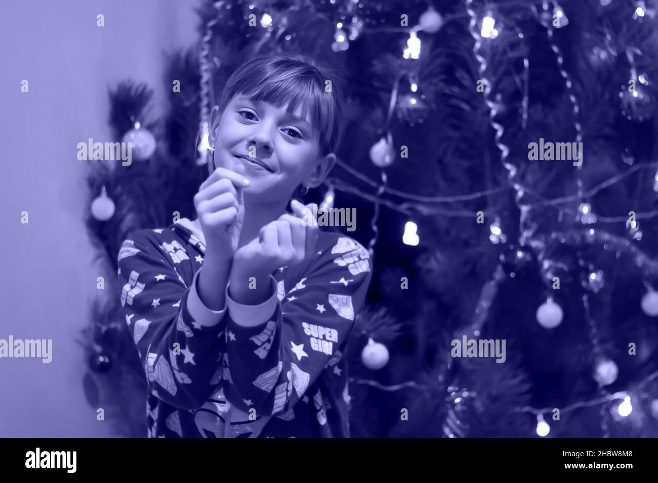 Defocus petite blonde caucasienne fille de 10 ans dans les stands de pyjama près de l'arbre de Noël.Affiche le symbole coeur coréen, symbole amour.Couleur de l'année Banque D'Images