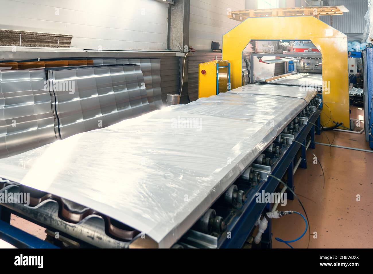 Tapis convoyeur avec production de tuiles de toit en métal fini et emballé dans l'intérieur de l'entrepôt de l'usine. Banque D'Images