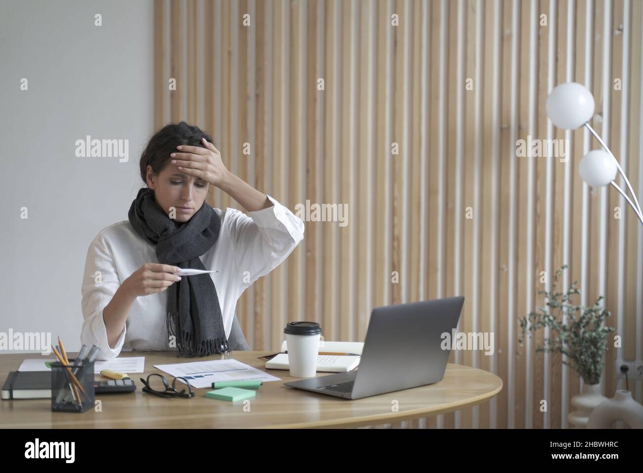 Femme fatiguée indépendante assise au bureau à la maison regardant malade au thermomètre numérique Banque D'Images