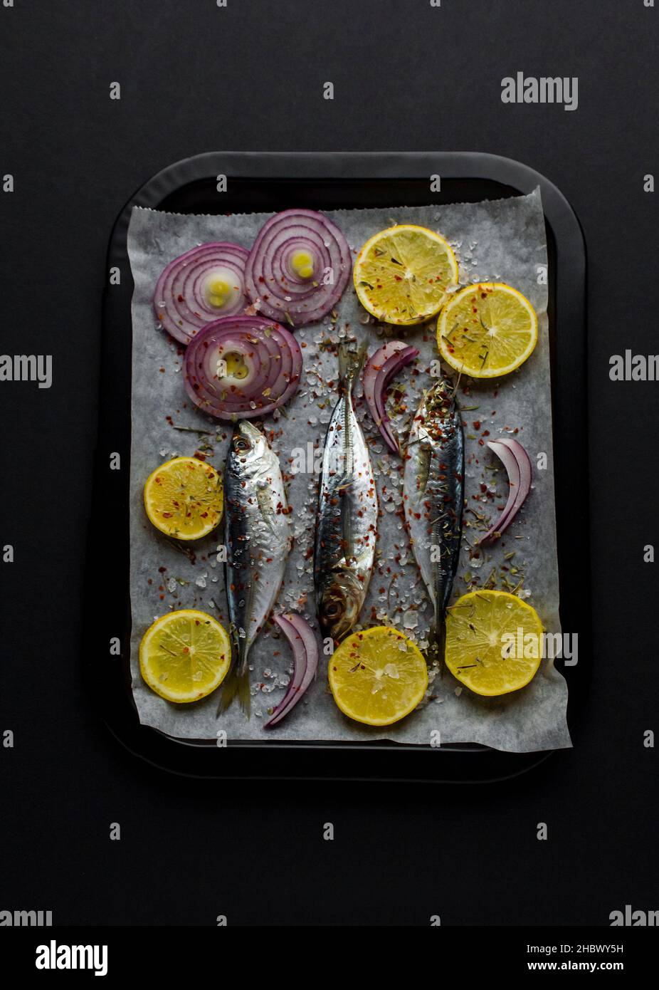 Poisson non cuit de maquereau de cheval, istacrit sur du papier de cuisson au four avec des tranches d'oignon violet, de poivron rouge et de citron prêt à cuire. Image verticale Banque D'Images