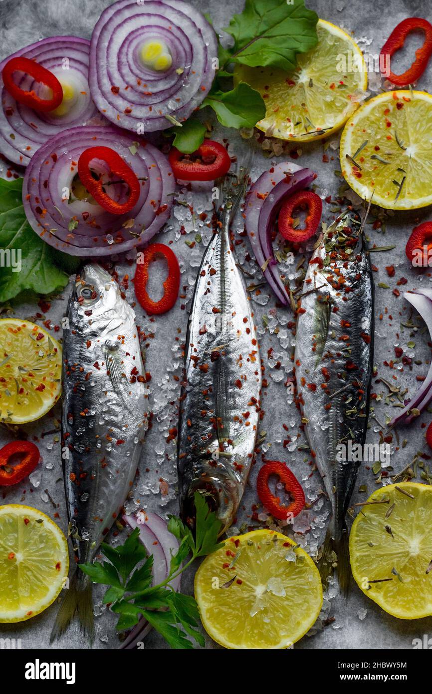 Poisson non cuit au maquereau, à l'istacrit sur du papier de cuisson au four avec des tranches d'oignon violet, de poivron rouge et de citron prêt à cuire. Banque D'Images