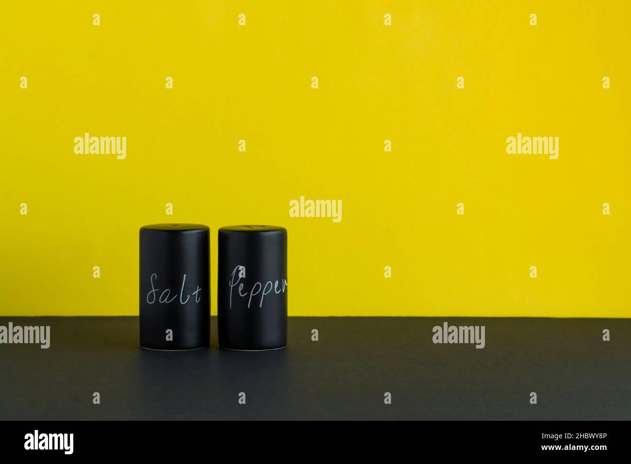 Salières et poivrières se trouvent sur le sol noir, devant la couleur jaune fluorescent.sel et poivre en les essorant par des lettres blanches. Banque D'Images