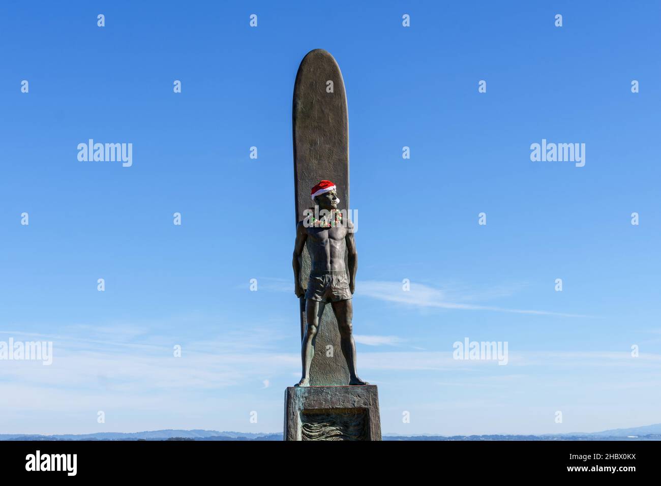 Statue du surfeur, monument du surf, bronze d'un surfeur mâle debout devant sa planche décorée de Santa Hat et de vacances leis pour Christma Banque D'Images