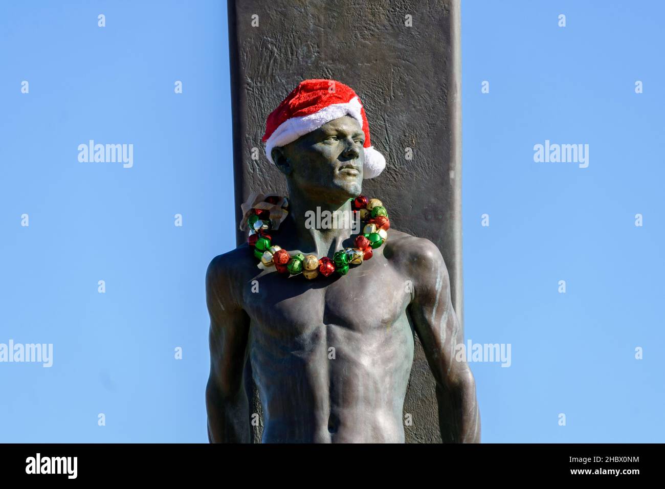 Statue du surfeur, monument du surf, bronze d'un surfeur mâle debout devant sa planche décorée de Santa Hat et de vacances leis pour Christma Banque D'Images