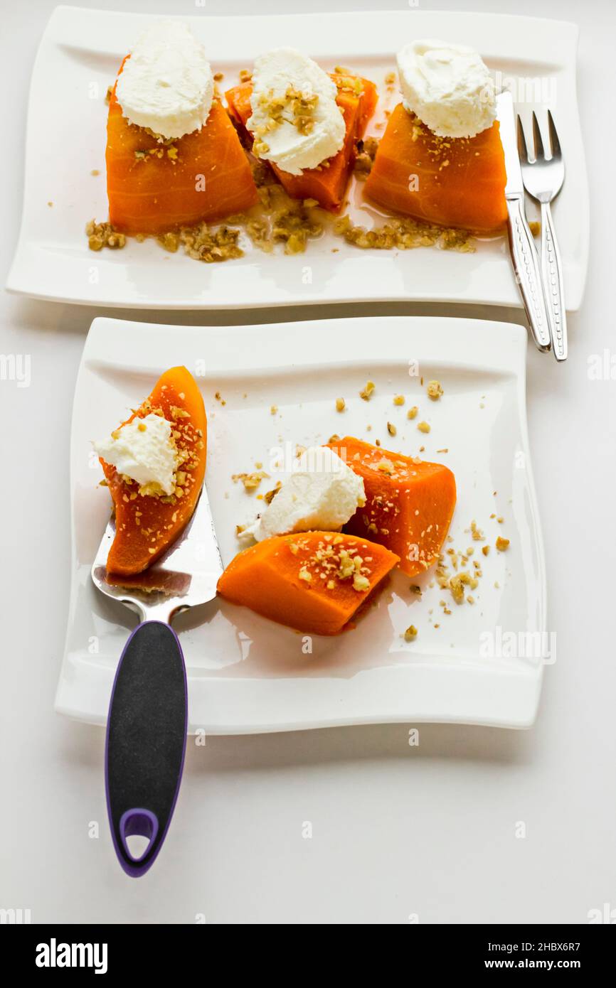 Citrouille turque traditionnelle dessert sur la surface blanche avec une spatule en métal. Garniture à la crème et aux noix hachées. Image verticale Banque D'Images