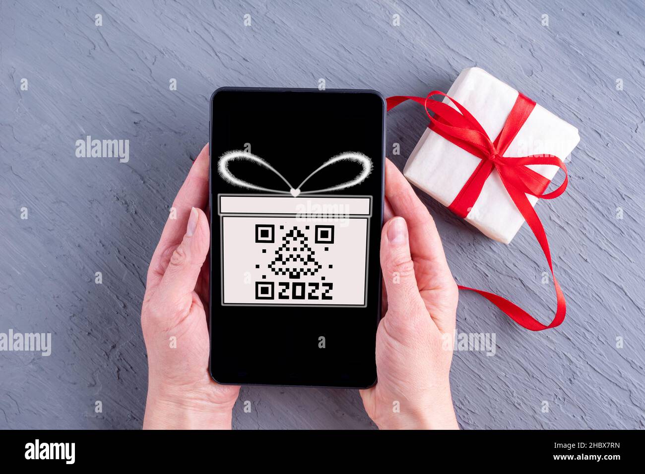 Mains tenant un téléphone portable avec un écran noir avec une boîte cadeau dessinée et un code qr en forme d'arbre de Noël et une boîte cadeau avec un ruban rouge Banque D'Images