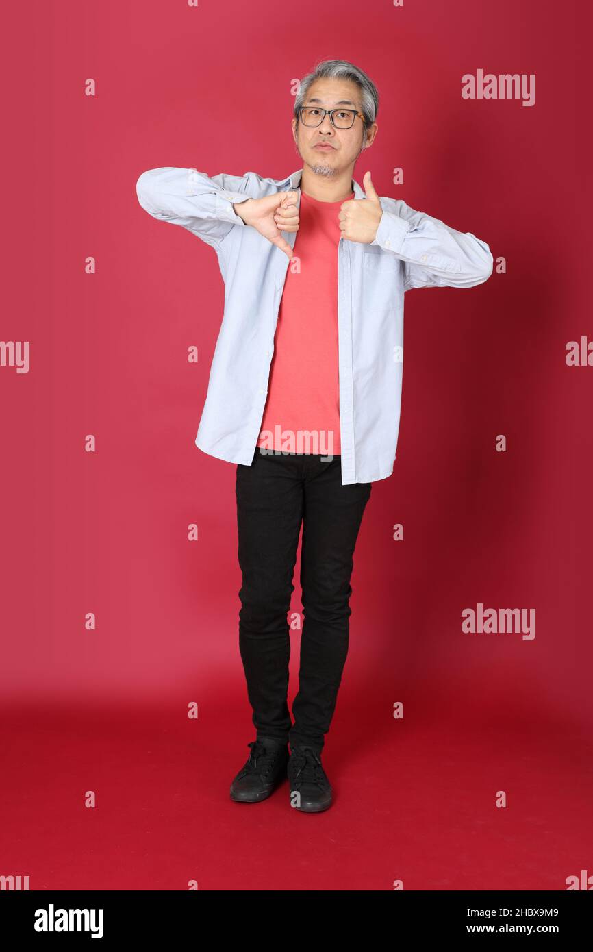 L'homme asiatique senior portant une chemise bleue avec de longs cheveux debout sur fond rouge. Banque D'Images