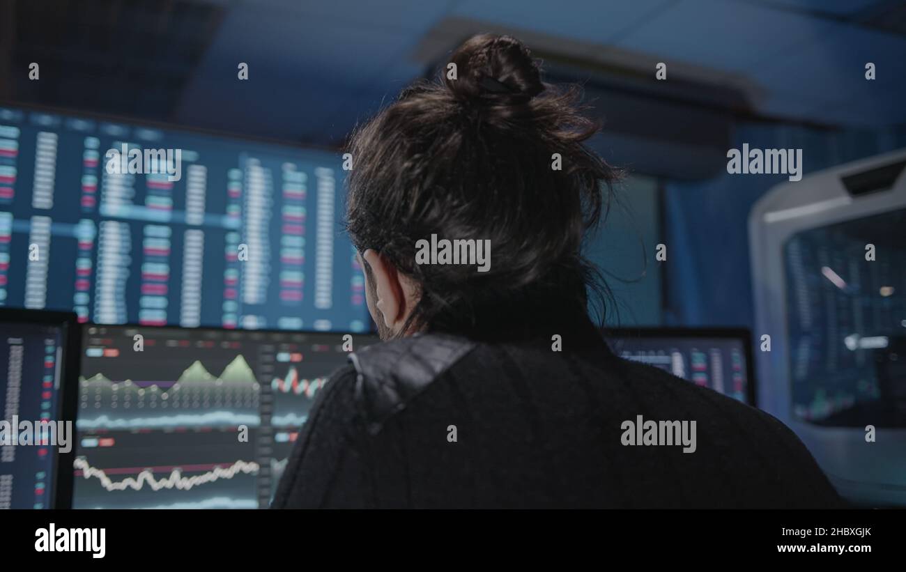 Jeune homme de barbe longue et à cheveux longs effectuant une analyse pour le trading de jour sur les écrans d'analyse de crypto-monnaie Banque D'Images