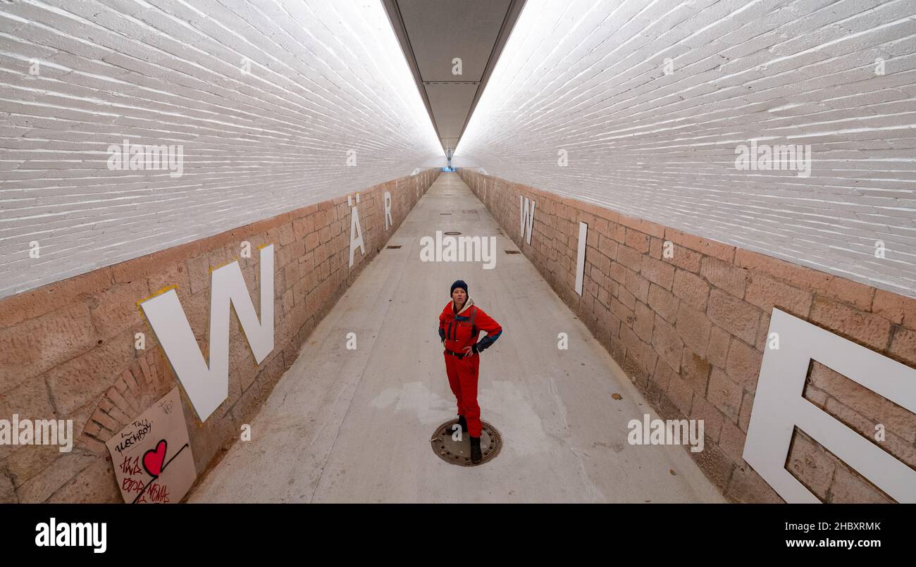 22 décembre 2021, Saxe, Chemnitz : l'artiste Anke Neumann se trouve dans le nouveau tunnel piétonnier de la gare centrale de Chemnitz.Le tunnel étroit entre le centre-ville et le quartier de Sonnenberg est en cours de modernisation, entre autres, par un nouveau concept d'éclairage.En outre, des lettres blanches de 1,40 mètres de haut sur les murs forment une citation de la chanson 'Wie ich' du groupe Kraftklub: 'ICH wär'gern weniger wie ich, ein bisschen mehr so wie du'.Dans le vernaculaire, le sous-passage de 220 mètres de long, auparavant plutôt sombre, est communément appelé le « tube germinatif ».En deux phases de construction, l'entra Banque D'Images