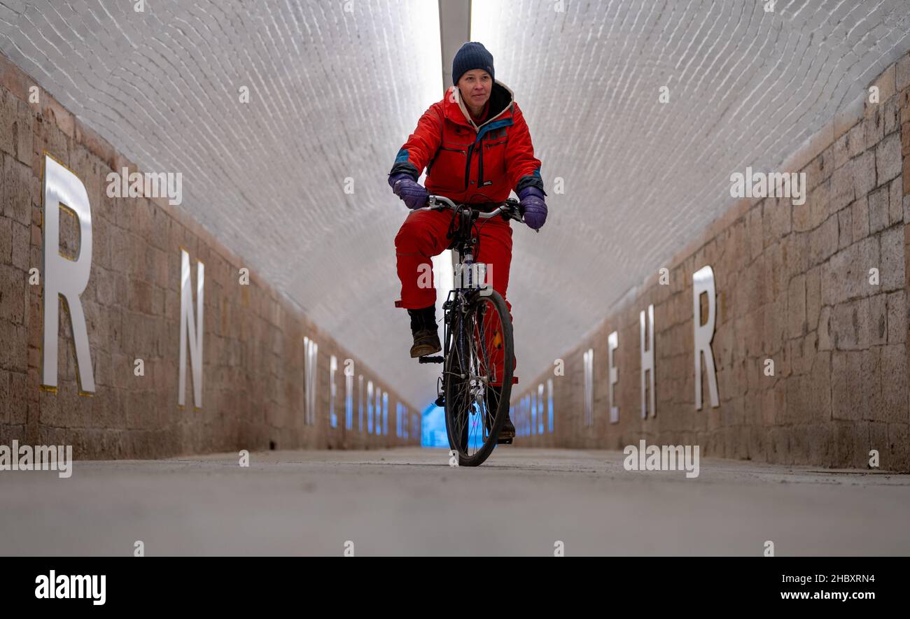 22 décembre 2021, Saxe, Chemnitz: L'artiste Anke Neumann conduit son vélo dans le nouveau tunnel piétonnier de la gare centrale de Chemnitz.Le tunnel étroit entre le centre-ville et le quartier de Sonnenberg est en cours de modernisation, entre autres, par un nouveau concept d'éclairage.En outre, des lettres blanches de 1,40 mètres de haut sur les murs forment une citation de la chanson 'Wie ich' du groupe Kraftklub: 'ICH wär'gern weniger wie ich, ein bisschen mehr so wie du' ('je voudrais être moins comme moi, un peu plus comme vous').Dans le vernaculaire, le passage inférieur de 220 mètres de long, auparavant plutôt sombre, est connu par le peuple Banque D'Images