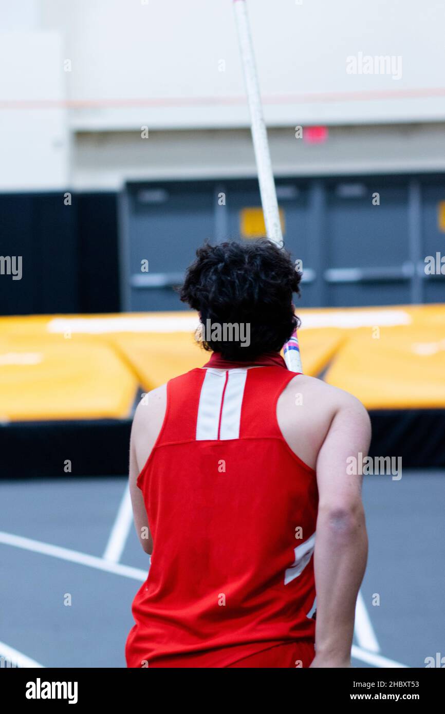 Un athlète d'école secondaire sur la piste avec un poteau dans ses mains et les matts dans l'arrière-plan prêt à pole voûte lors d'une compétition en intérieur. Banque D'Images