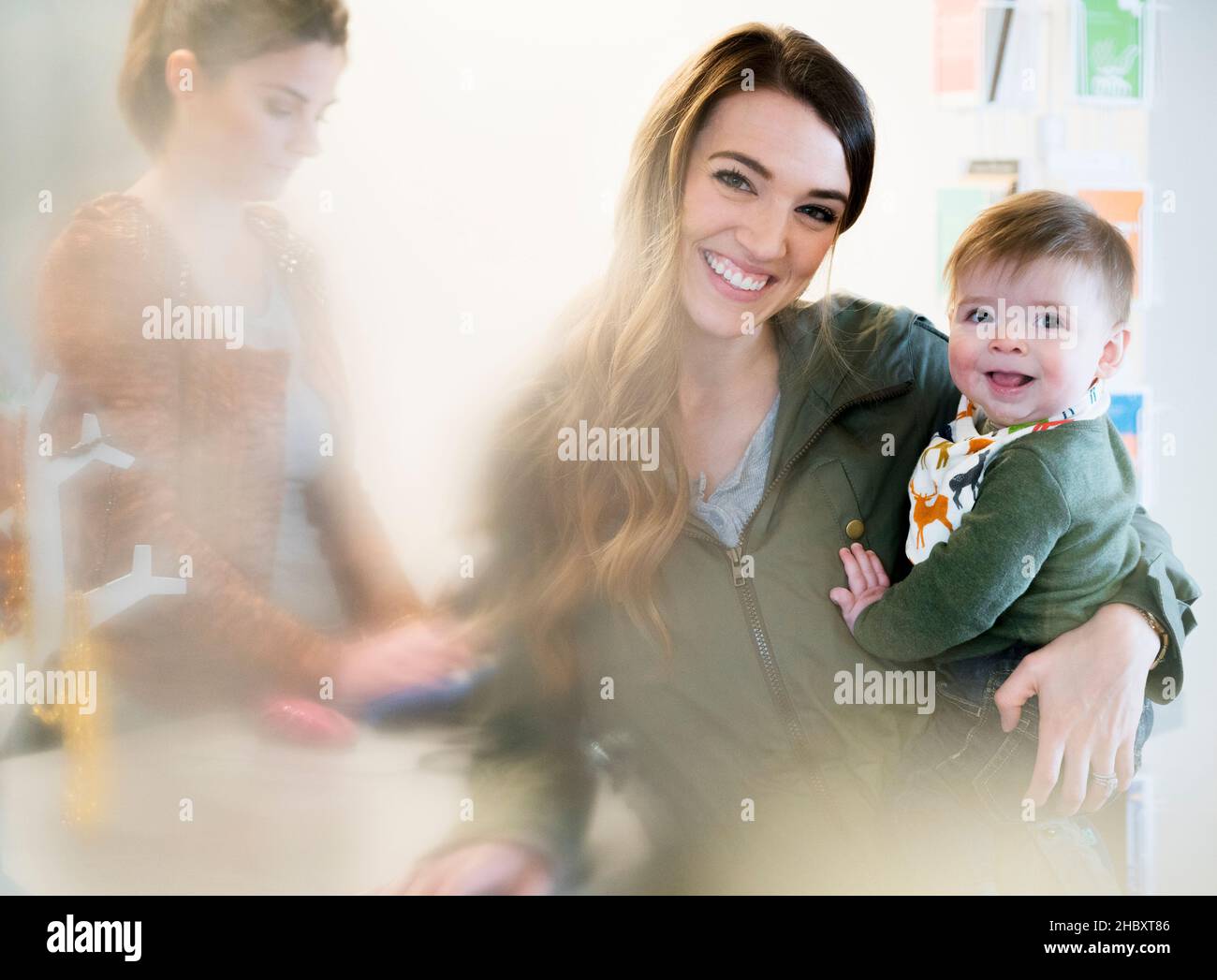 Femme tenant un bébé debout à côté d'une caisse avec un assistant de magasin, souriant à la caméra. Banque D'Images