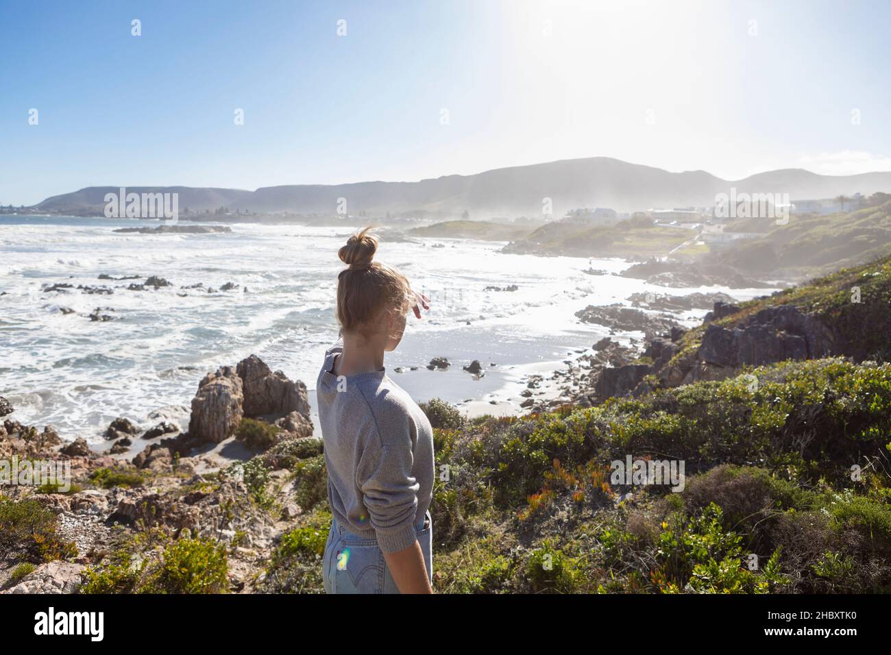 Une adolescente sur des rochers, regardant la côte, les vagues se brisent et la brume monte. Banque D'Images