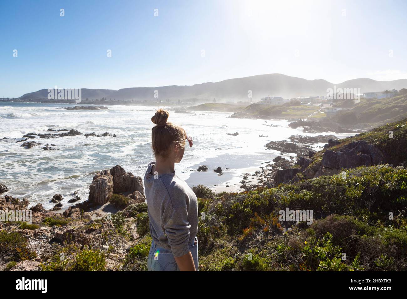 Une adolescente sur des rochers, regardant la côte, les vagues se brisent et la brume monte. Banque D'Images