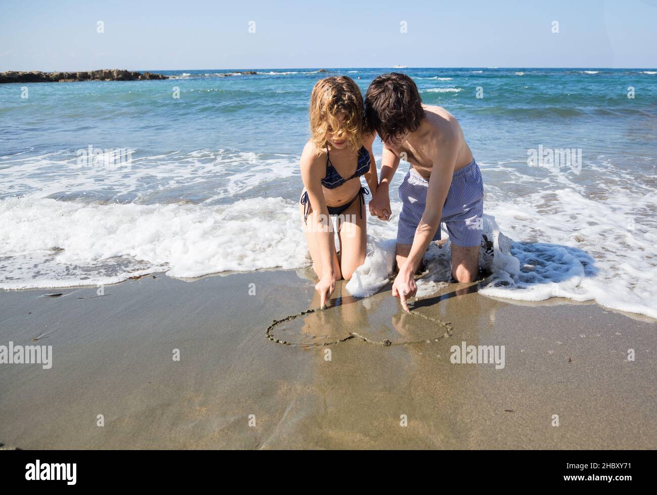 jeune femme et homme amoureux, dessinez un coeur sur le sable tout en étant assis sur la mer.Saint-Valentin en vacances, premier amour, bonnes relations, somme Banque D'Images