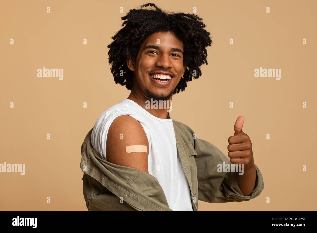 Être vacciné.Homme africain avec bande adhésive sur le bras montrant le pouce vers le haut Banque D'Images