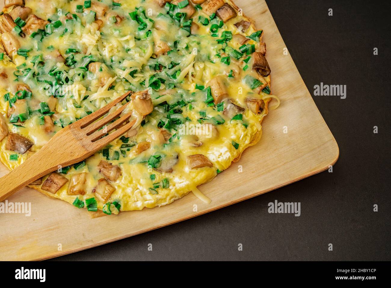 Omelette rustique avec oignon de printemps et parmesan sur une plaque en bois avec une fourchette en bois isolée sur noir, gros plan Banque D'Images