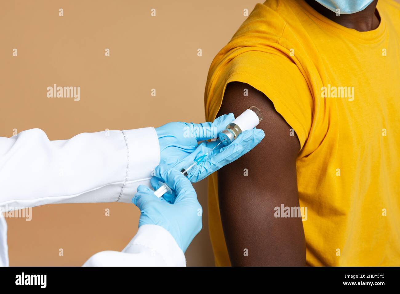 Médecin méconnaissable portant des gants médicaux bleus faisant la vaccination d'un patient masculin noir Banque D'Images