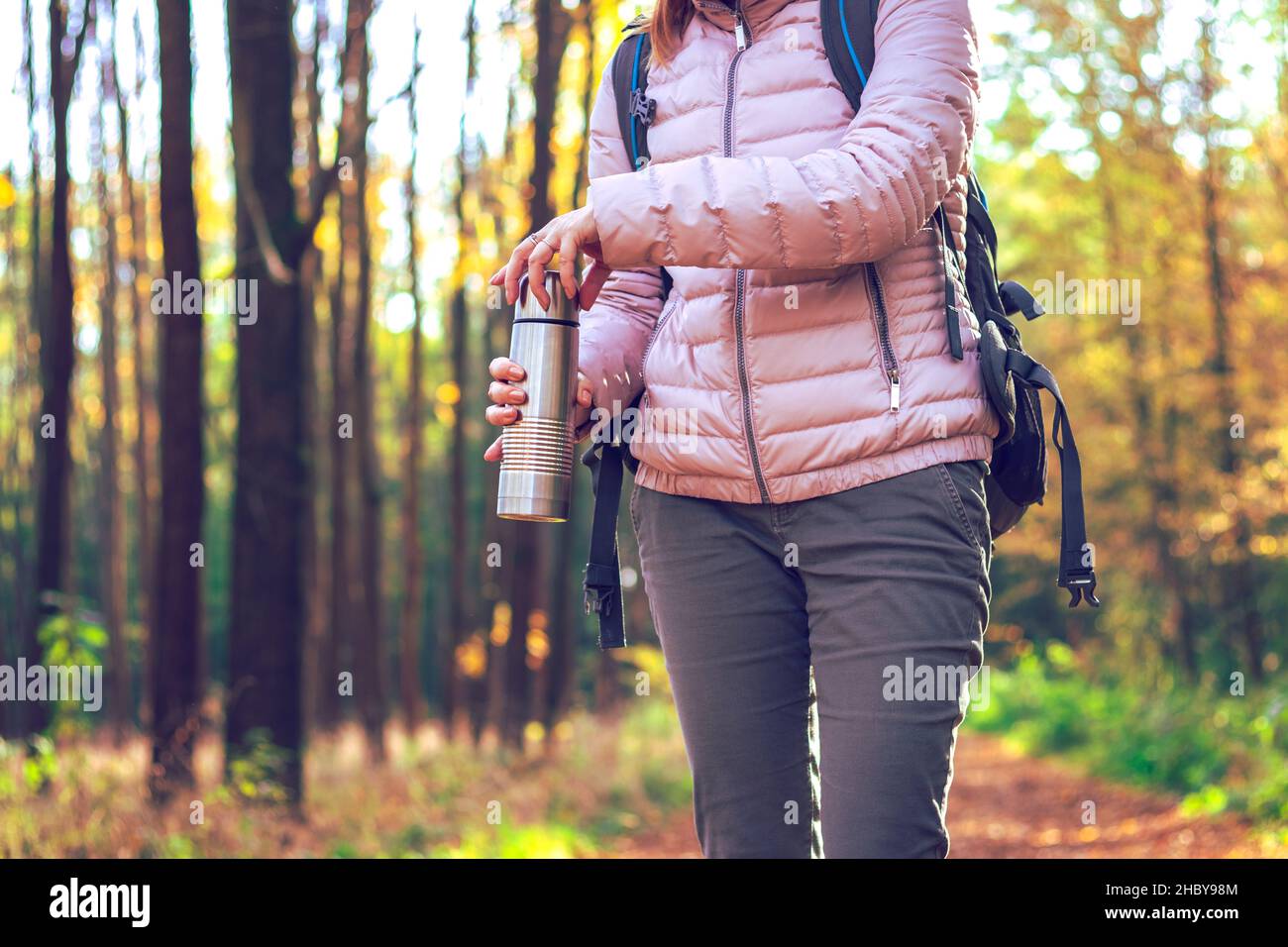 Rafraîchissements dans la forêt pendant la randonnée automnale.Femme voyageur avec sac à dos tenant un thermos Banque D'Images