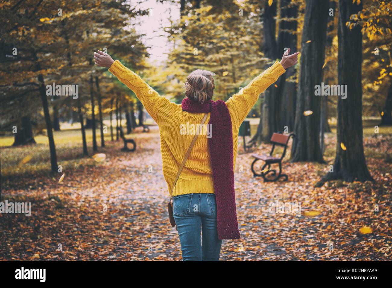 Bonne femme portant un chandail jaune, une écharpe rouge et un Jean.Parc public d'automne.Image en tons Banque D'Images