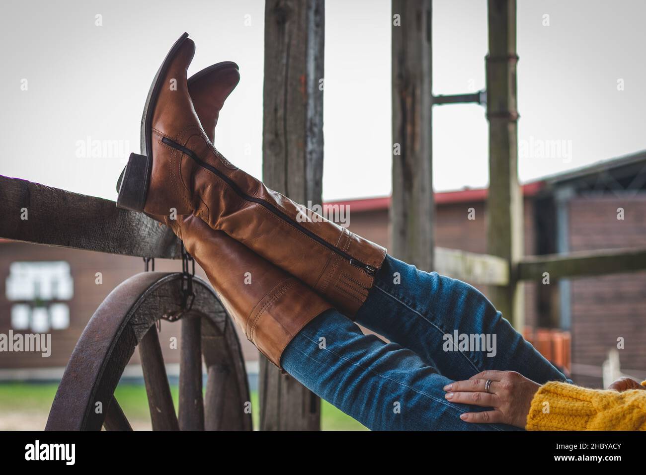 La femme se détend sur le ranch avec ses jambes sur une main courante en bois.Bottes en cuir et jeans Banque D'Images