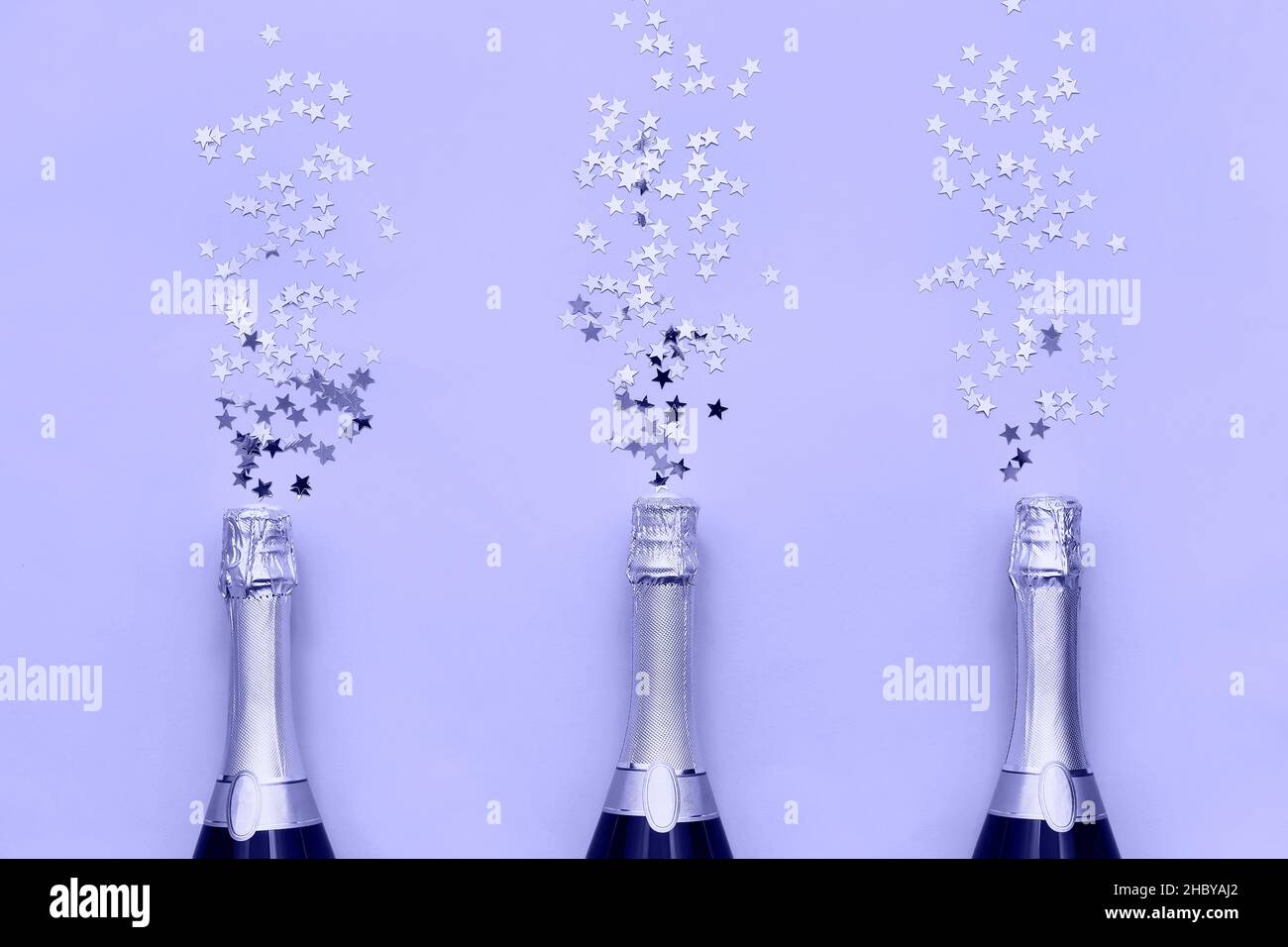 Trois bouteilles de champagne avec des étoiles confetti sur fond lilas très péri.Plat de l'anniversaire, de la Bachelorette, concept de célébration du nouvel an Banque D'Images