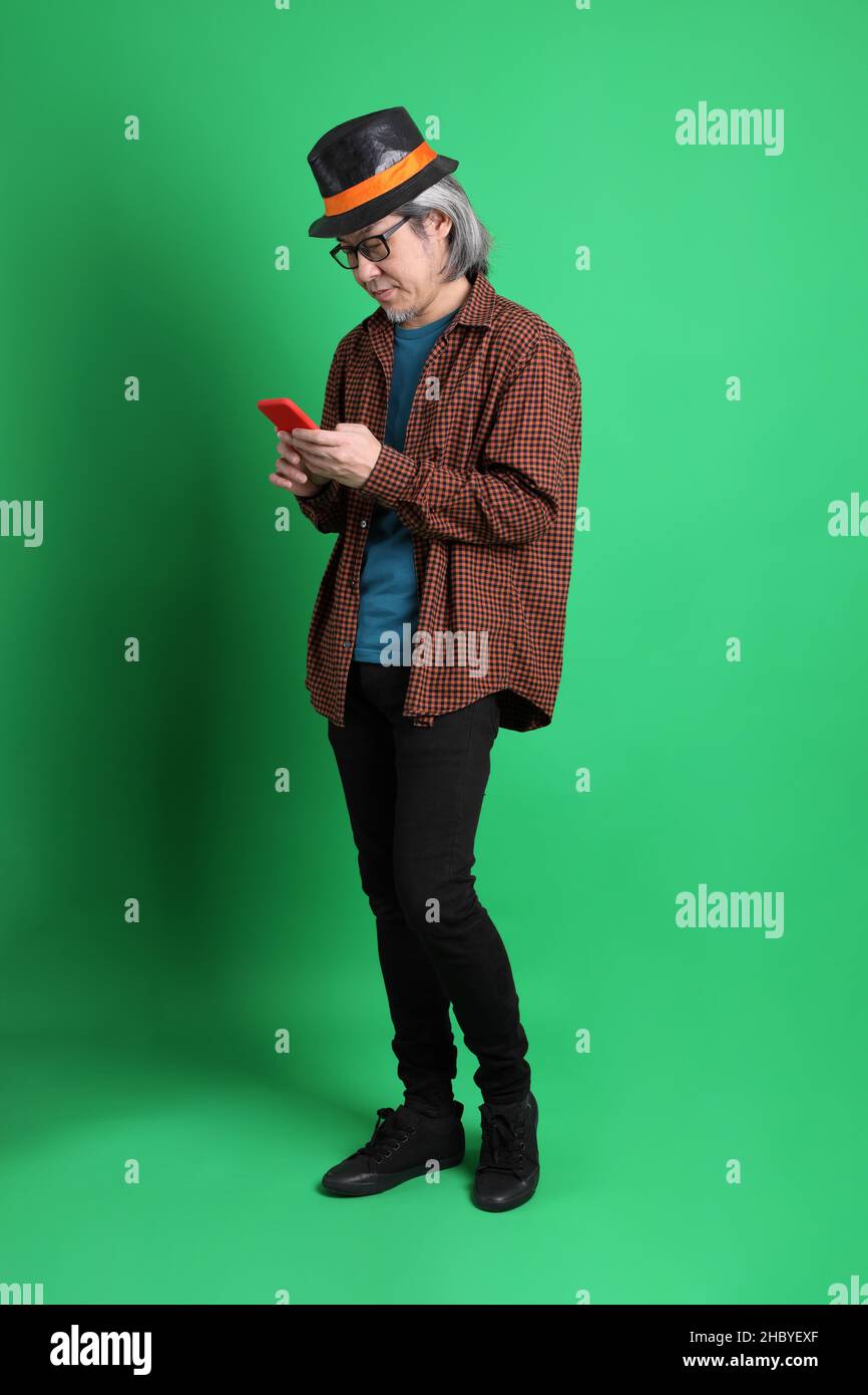 L'homme asiatique senior s'habille à thème de couleur de la saison de Thanksgiving, portant une chemise à carreaux orange et un chapeau noir debout sur fond vert. Banque D'Images