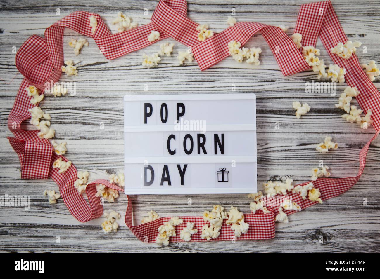 Visionneuse avec texte Popcorn Day parmi les popcorns et arrière-plan de ruban rouge festif.Vue de dessus.Style vintage. Banque D'Images