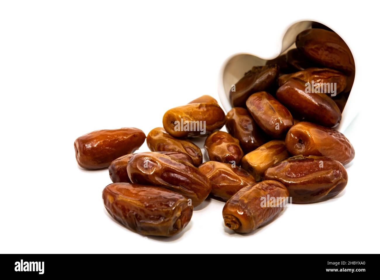 Les dates sont isolées.Les dates se déversent d'une tasse en forme de coeur sur un fond blanc gros plan.Fruits secs Banque D'Images