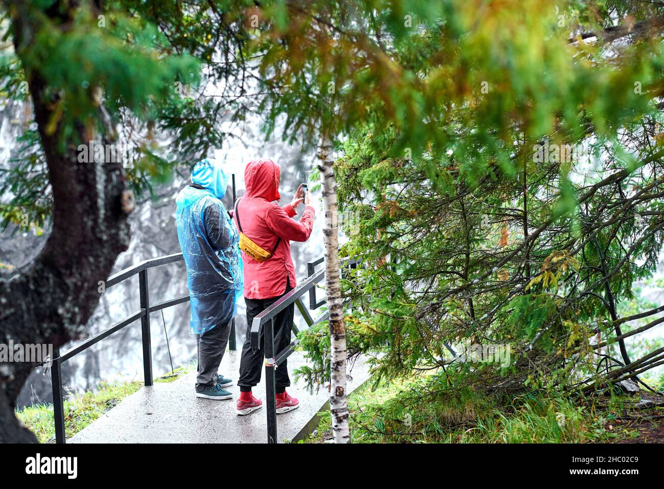 Un homme sous un imperméable bleu et une femme sous une veste rouge et des baskets rouges apprécient la vue à couper le souffle dans un parc de montagne parmi les conifères Banque D'Images