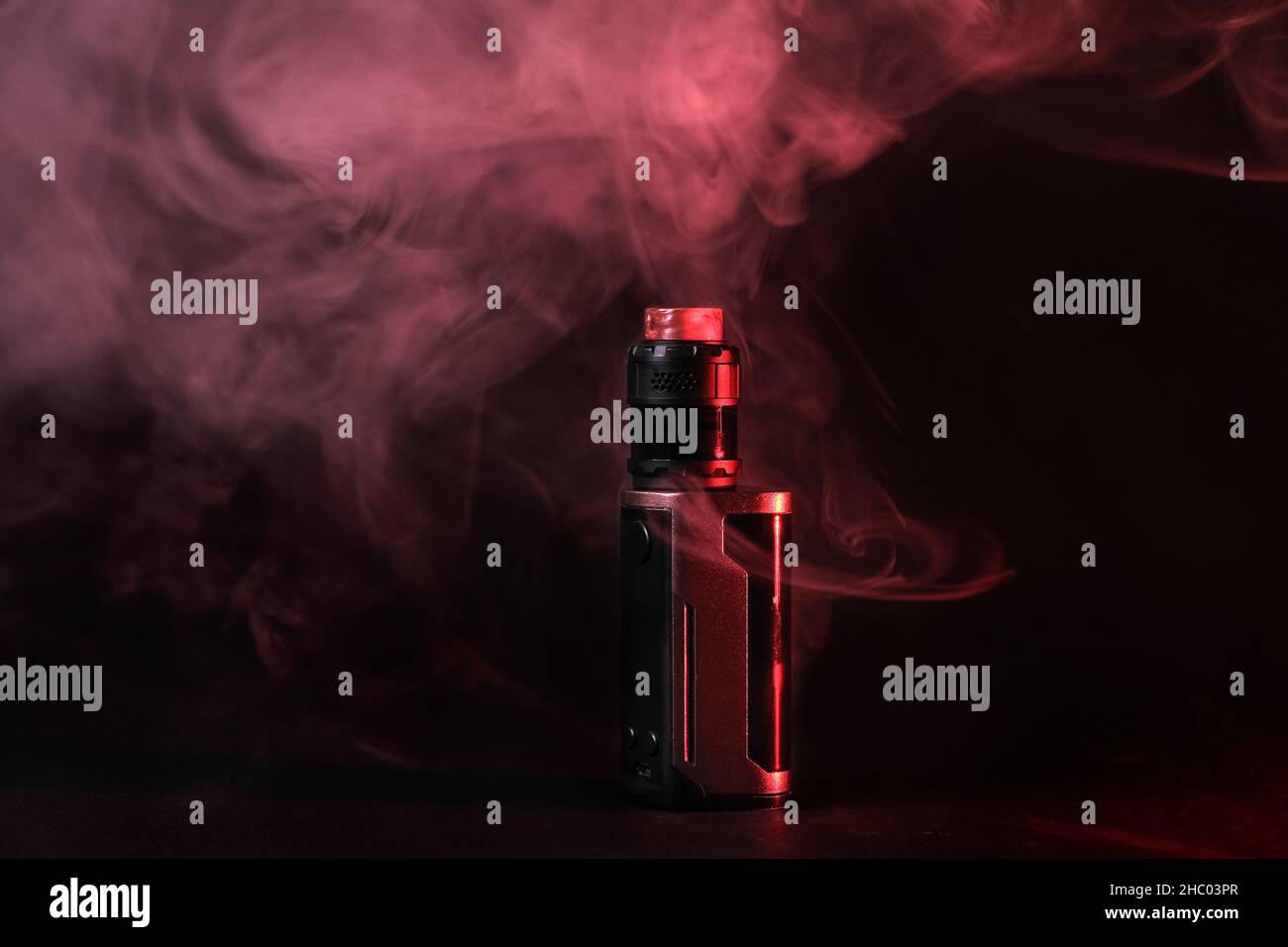 Dispositif de vapotage électronique mod, atomiseur se tient dans la fumée de vape et la vapeur illuminée par lumière rouge. Banque D'Images