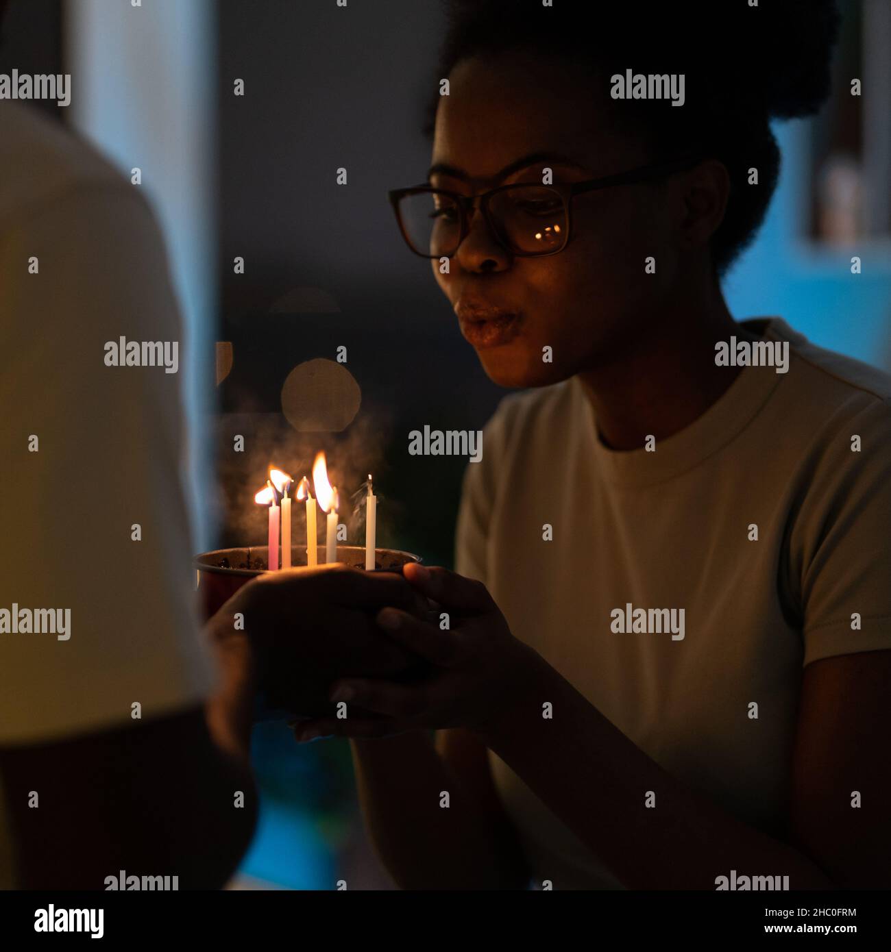 Jeune femme africaine heureuse soufflant des bougies sur un gâteau cuit par un mari bien-aimé pour l'anniversaire Banque D'Images