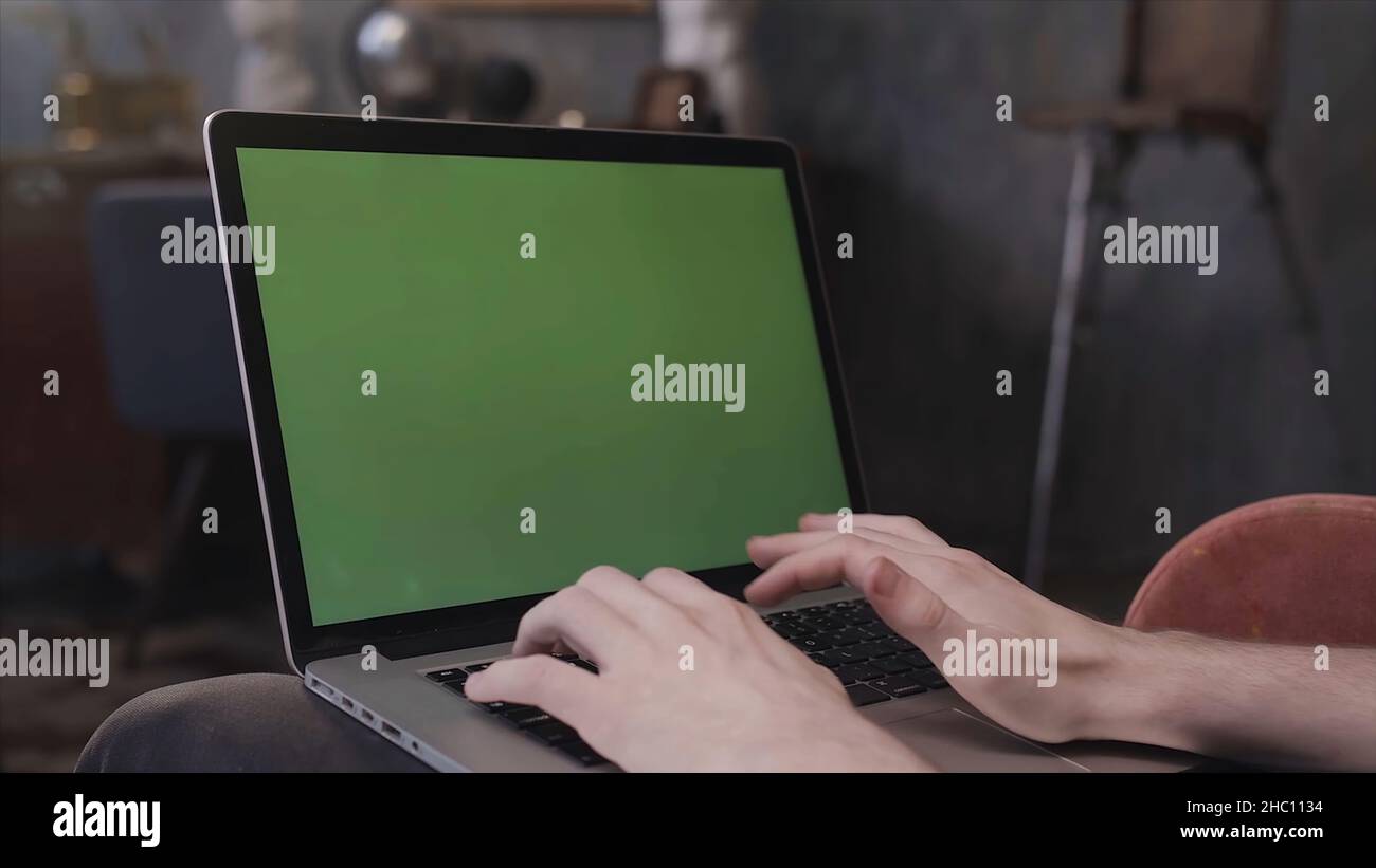 Vue sur l'épaule d'un homme assis à son bureau et travaillant sur un ordinateur portable avec écran vert.Homme utilisant un ordinateur portable avec clé chroma. Banque D'Images