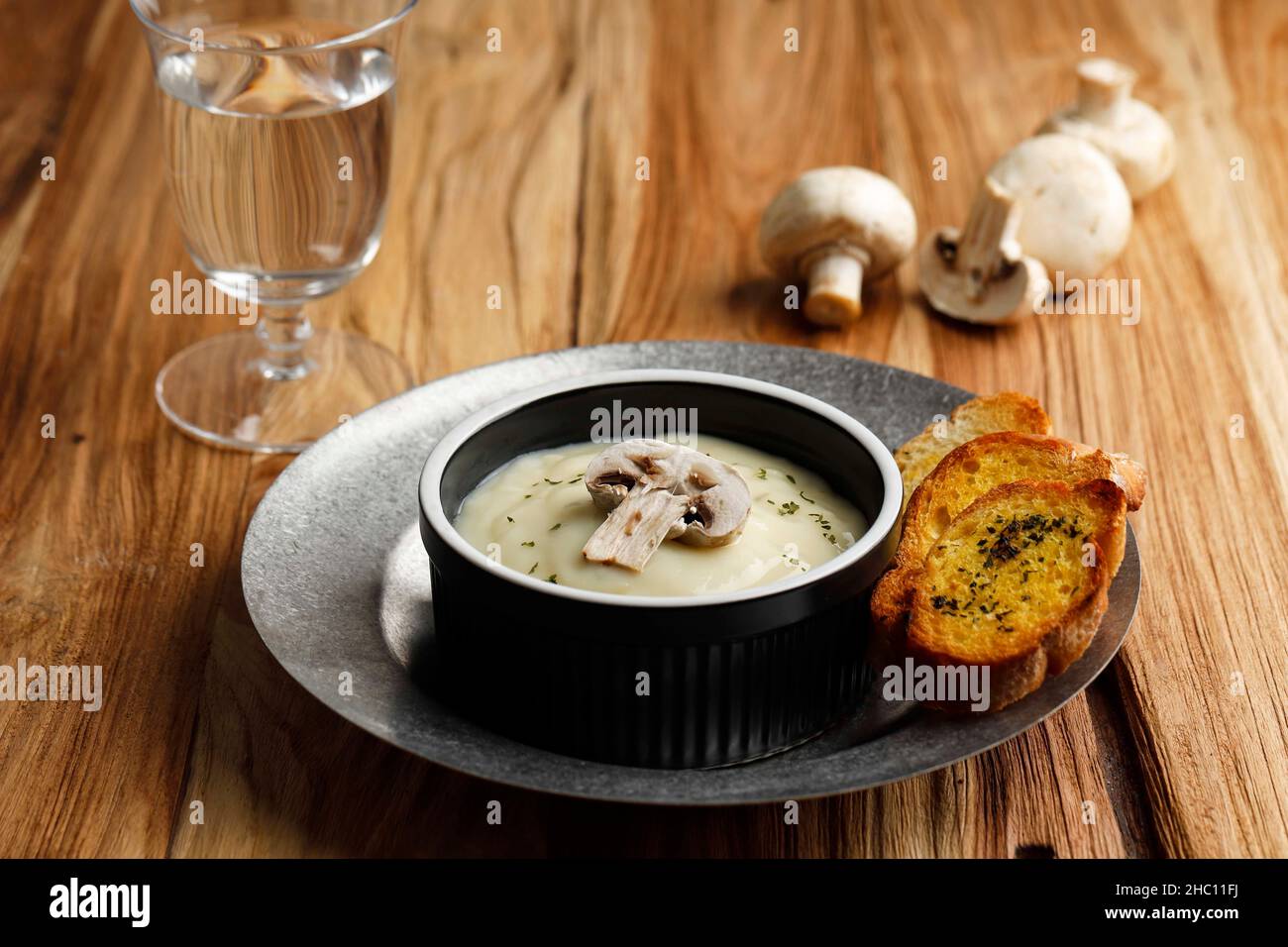 Soupe crémeuse aux champignons maison, avec baguette de pain à l'ail croustillant, servir sur un bol en céramique noire ou un raméquin au-dessus d'une table rustique. Banque D'Images
