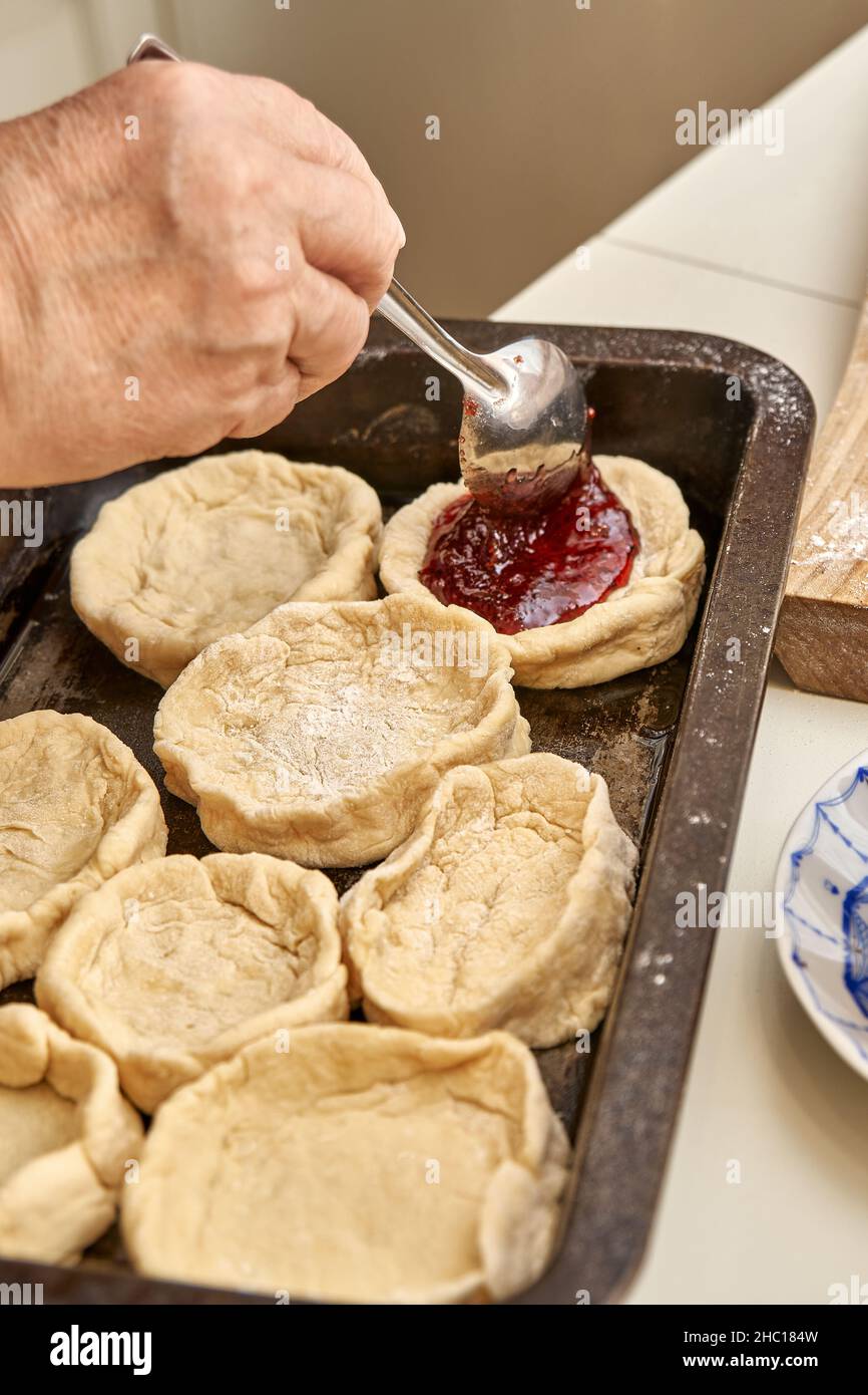 La femme senior remplit les tartes crues avec un dessert de cuisine de confiture de baies maison naturel à la table blanche dans la cuisine vue extrême Banque D'Images