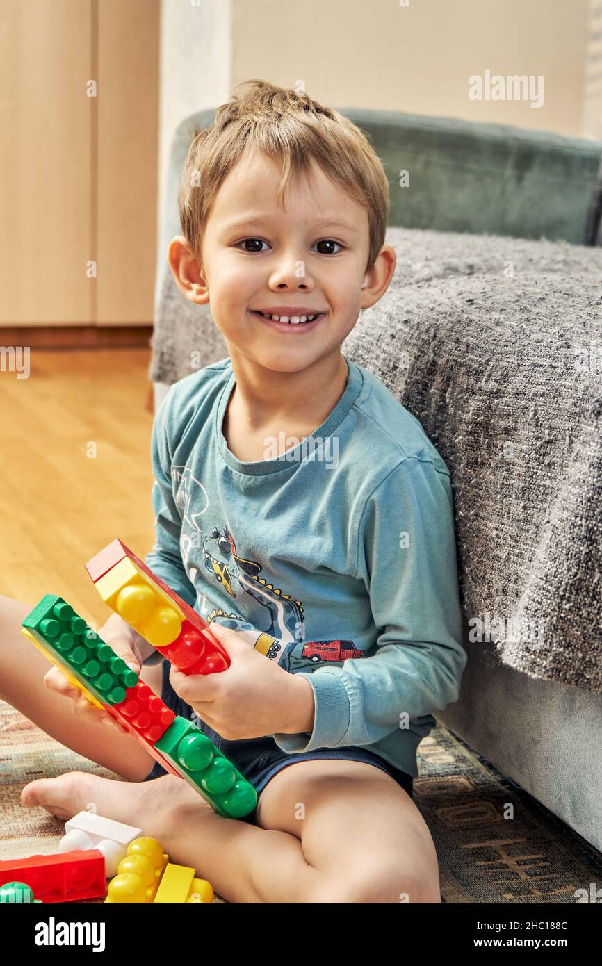 Joyeux pieds nus petit garçon tient des détails en plastique coloré  constructeur assis sur le tapis de sol près du canapé dans la salle de  séjour vue proche Photo Stock - Alamy