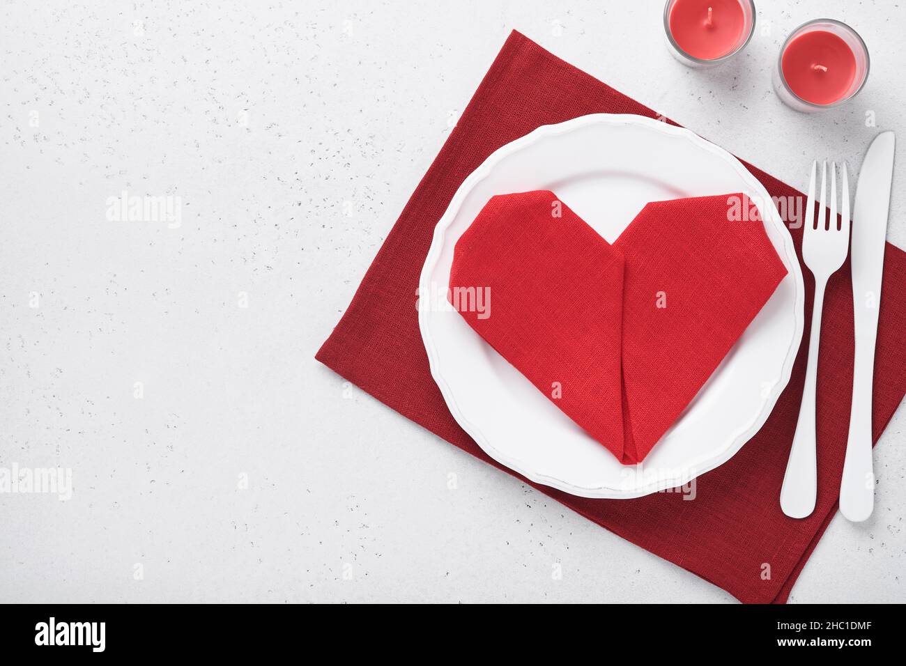 Table de jour de Valentinas couleur blanche avec argenterie blanche, serviette rouge pliée comme coeur, bougies, champagne, verres sur fond blanc pour greeti Banque D'Images