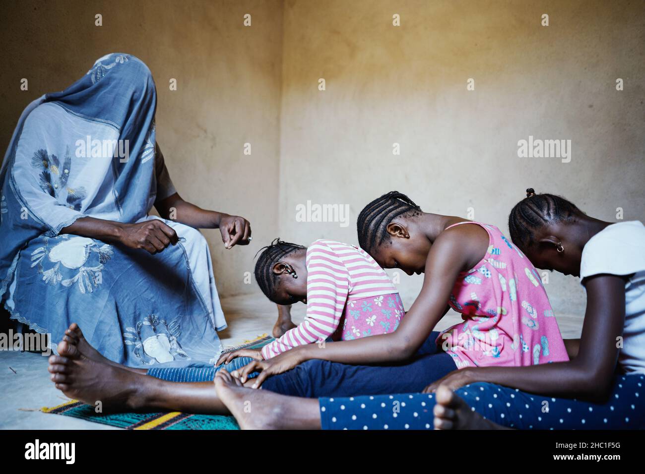 Personne totalement couverte tenant une lame parlant à un groupe de filles africaines noires intimidées assis dans une rangée sur le sol avec leur tête baissée pri Banque D'Images